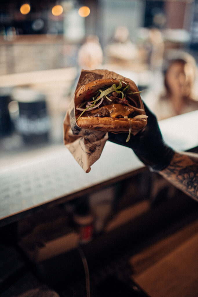 Hand in schwarzen Handschuhen hält einen appetitlichen Burger, serviert bei einem Catering-Event in Osnabrück