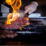 Burgerpatties werden auf einem Grill mit hoher Flamme zubereitet, wobei die Flamme das Fleisch leicht anröstet